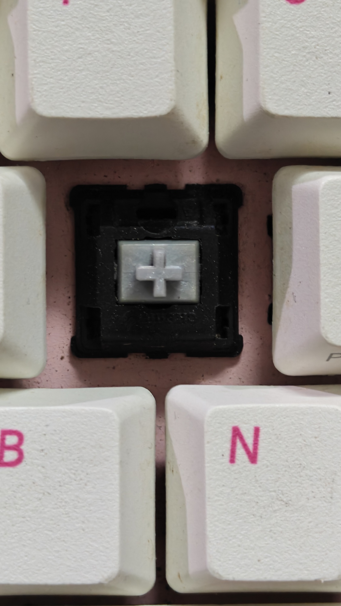 Varmilo Miya68 Pro - Pink 6 Cận cảnh một switch linear màu trắng đã tháo keycap trên nền vỏ phím hồng.